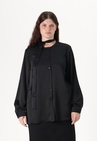 Black, long-sleeve blouse with button closure, satin finish, and a tied neck ribbon. Features rounded collar and slightly sheer sleeves.
