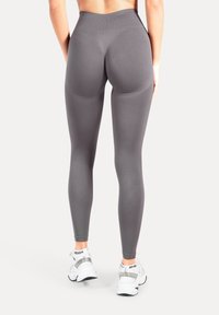 Leggings grigie a vita alta con una texture liscia e cuciture sagomate, abbinate a scarpe da ginnastica bianche. Vista posteriore che mostra la vestibilità e il design.