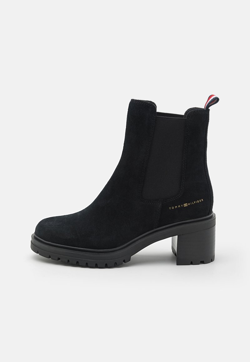 Bottine en daim noir avec talon bloc, panneau latéral élastique, languette avec bandes rouges, blanches et bleues, et petit logo doré Tommy Hilfiger.