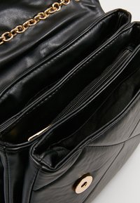 Borsa a tracolla nera in ecopelle con design trapuntato, dotata di hardware in oro e molteplici scomparti, incluso un taschino con zip.