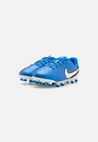 Modré futbalové kopačky s textúrovanym povrchom, bielymi akcentmi a čiernym logom Nike. TPU podrážka s modrými kolíkmi pre lepšiu priľnavosť na trávnatých povrchoch.