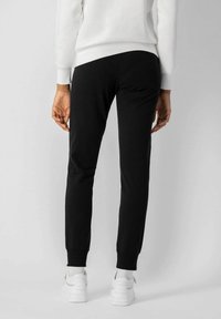 Pantalones jogger negros hechos de tela suave, ajustados en los tobillos, combinados con zapatillas blancas. Diseño sencillo sin acentos ni patrones visibles.