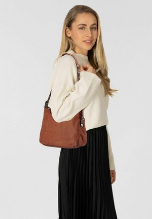 Borsa a mano in pelle marrone con texture morbida, forma rettangolare e dettagli decorativi sulle cinghie. Indossata a spalla, abbinata a un maglione.