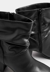 Mustat nahkasaappaat nilkkamallilla, joissa on löysä muotoilu, sivuzipperi ja paksu korko. Suloinen tekstuuri hienovaraisilla yksityiskohdilla.