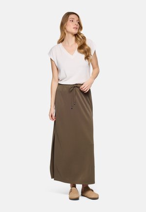 Mujer con cabello largo y ondulado, vestida con una blusa blanca de manga corta y cuello en V, falda larga verde oliva con abertura lateral y zapatos beige sin cordones.