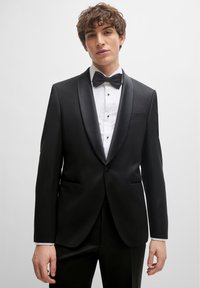 Black tuxedo jacket with satin lapels, white shirt, and bow tie. Features two front pockets and a single button closure. Classic design.