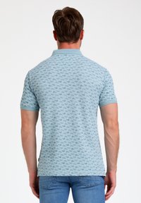 Camisa polo azul cielo con un patrón repetitivo, de manga corta y acabado texturizado. Cuenta con un cuello y puños acanalados.