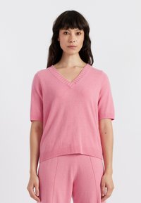 Maglione a maniche corte con scollatura a V in morbido maglione rosa, caratterizzato da polsini e orlo a coste, offre una vestibilità rilassata e una texture liscia.