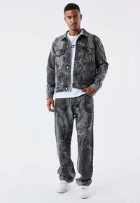 Chaqueta y pantalones de denim gris con un patrón floral blanco, combinados con una camiseta blanca. Zapatillas blancas complementan el atuendo.