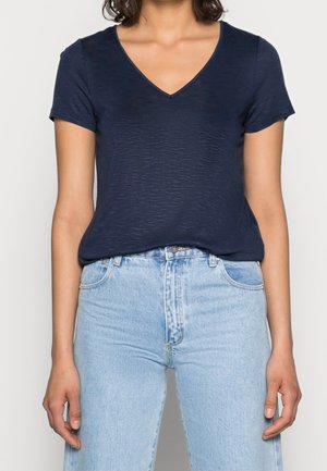 T-shirt bleu marine à manches courtes avec un col en V, fabriqué en tissu texturé, associé à un jean taille haute bleu clair.