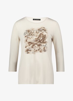 Kremowa koszula z długim rękawem z nadrukiem tekstowym: "GLITTER", "glam" i "SPARKLE" oraz brązowe buty na wysokim obcasie ozdobione kryształkami.