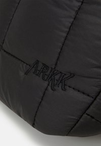 Czarna pikowana torba z przeszyciami i wyraźnym czarnym logo "ARKK". Gładka, matowa tkanina.