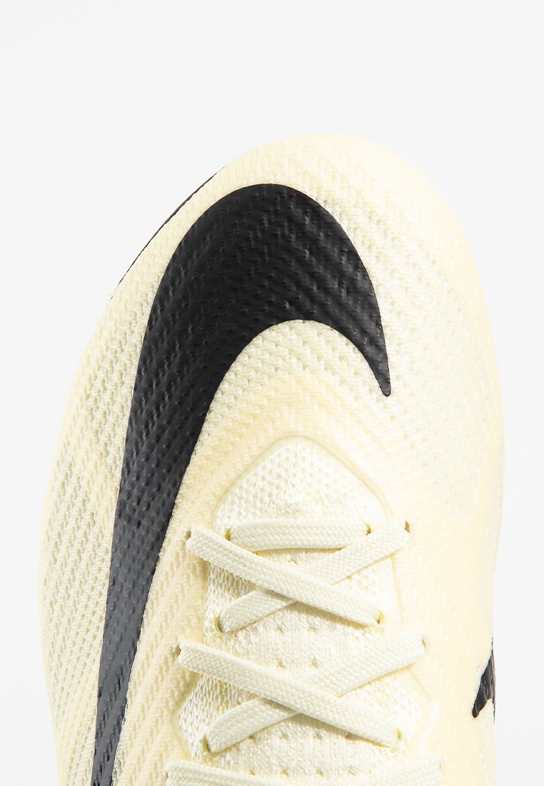 Baskets de couleur crème avec une tige texturée, présentant un emblème Nike swoosh noir proéminent et des lacets. Des motifs géométriques décorent la surface.