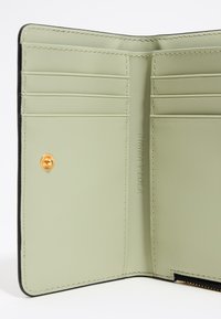 Intérieur d'un portefeuille en cuir vert comprenant plusieurs fentes pour cartes, un bouton pression doré et une marque embossée. Texture lisse avec des coutures renforcées.