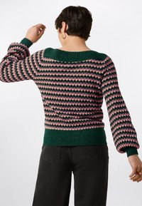 Knit sweater with a green ribbed collar and cuffs, featuring a multicolored zigzag pattern in pink and green. Soft texture, fitted style.