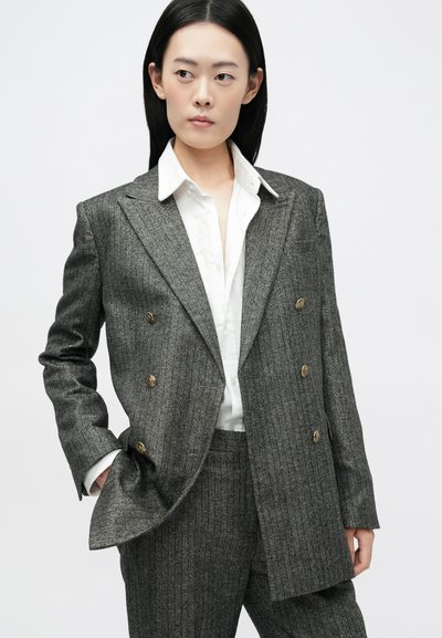 Sivi prugasti dvoredni sako s zlatnim gumbima, uparen s bijelom košuljom. Tkanina ima teksturiran uzorak i strukturirani dizajn.