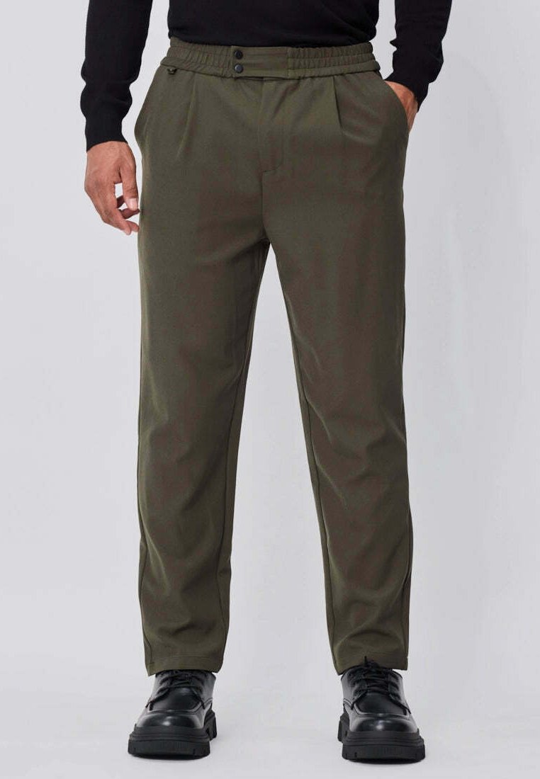 Pantalon vert olive avec plis, une taille élastique confortable, deux poches avant et une coupe fuselée, associé à des chaussures noires à lacets.
