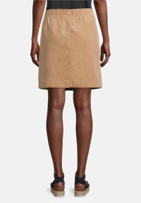 Kaki bomullskjol med elastisk midja, knälängd, slät textur och utan synliga mönster. Bärs med svarta platåsandaler.