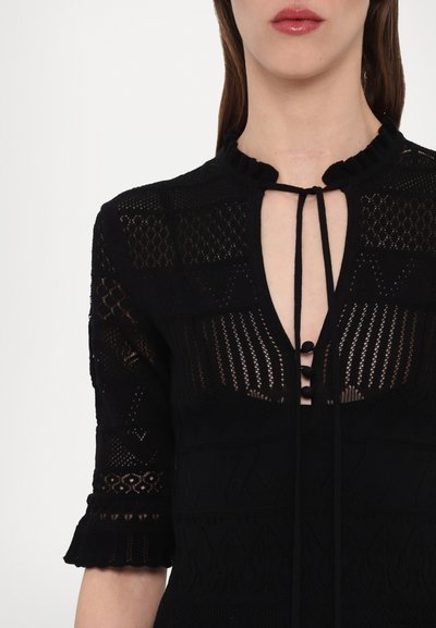Schwarzes gestricktes Oberteil mit kurzen Ärmeln, einem gewellten Ausschnitt und einem tiefen V-Ausschnitt mit Bindebändern und Knopfakzenten. Strukturierter Musterverlauf über das gesamte Oberteil.