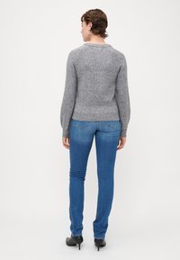 Grå strikket sweater med rund hals og lange ærmer, parret med blå tætsiddende jeans og sorte hæle. Subtile teksturer og detaljer synlige.