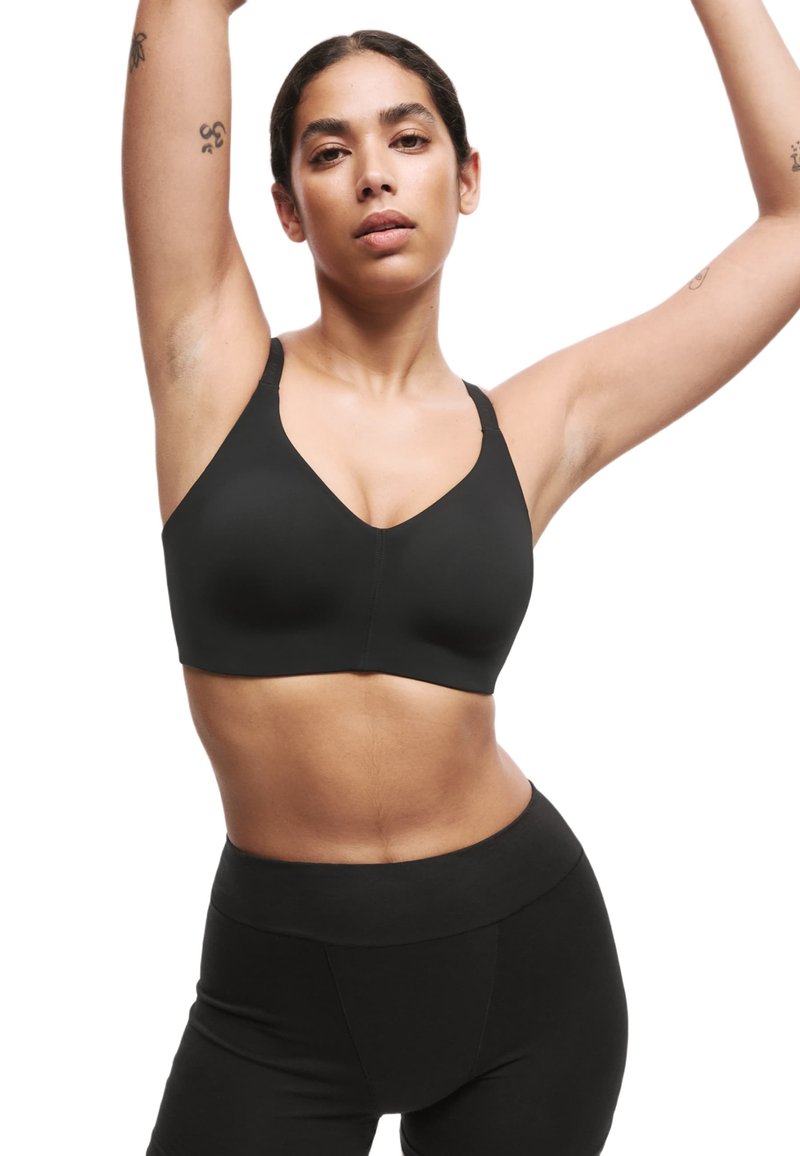 Soutien-gorge de sport noir avec un design en V, bretelles larges et texture lisse. Associé à des leggings noirs taille haute.