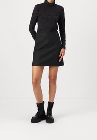 Top negro de cuello alto con patrón de cebra, combinado con una falda acampanada gris y botas de tobillo negras con cordones y suelas gruesas.