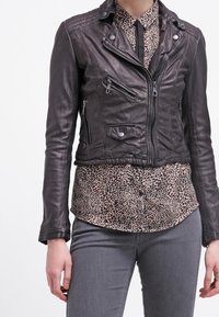 Læderbikerjakke i mørkebrun med lynlåse og trykknapper; lagdelt over en leopardmønstret bluse; model iført grå jeans.