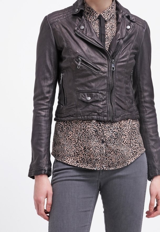 Læderbikerjakke i mørkebrun med lynlåse og trykknapper; lagdelt over en leopardmønstret bluse; model iført grå jeans.