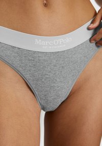 String gris à côtes avec une large ceinture blanche portant le logo, présentant "Marc O'Polo EST. À STOCKHOLM" imprimé en gris clair.