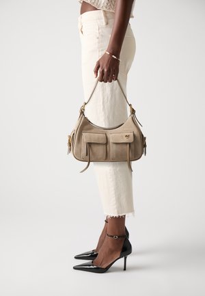 Beige suede handbag with two front pockets, slim straps, and gold hardware details. Paired with white cropped jeans and black heels.