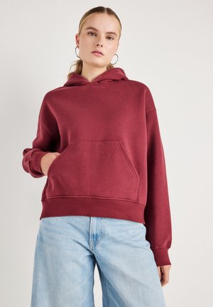 Sweat à capuche bourgogne avec une poche avant, cordon de serrage et poignets côtelés. Associé à un jean large bleu clair. Tissu doux et décontracté.