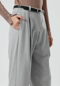 Grijze, op maat gemaakte broek met een losse pasvorm, gemaakt van gestructureerde stof. Voorzien van zijzakken en een zwarte riem met een zilveren gesp.