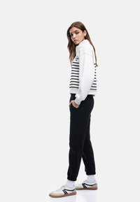Hvid- og sortstribet sweatshirt, sorte joggerbukser, hvide sneakers med sorte detaljer og opsmøgede ærmer, der viser et afslappet atletisk look.