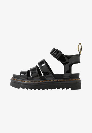 Black patent leather sandals with multiple straps, adjustable buckle, and orange stitching on platform sole featuring a zigzag texture.