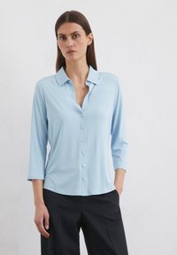 Light blue shirt with a collared neckline, buttons down the front, and three-quarter sleeves, made from a soft, smooth fabric.