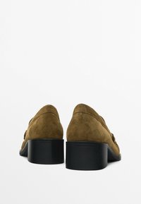 Ruskean mokkanahka kengät, joissa on matala, paksu musta korko ja pyöreä varvas. Sivussa on ommeltu yksityiskohtia.