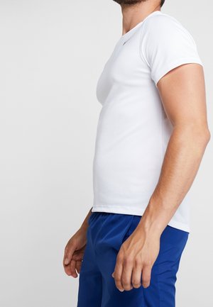 Biała koszula krótkim rękawem o dopasowanym kroju, wykonana z gładkiego materiału z okrągłym dekoltem, w zestawie z niebieskimi szortami sportowymi.