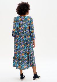 Robe maxi florale bleu foncé avec des motifs multicolores, manches longues, bordure à volants, portée avec des baskets montantes noires.