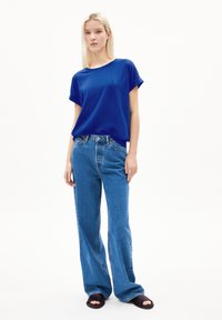 Blauwe T-shirt met korte mouwen en opgerolde boorden, gecombineerd met hoge blauwe flare jeans. Model draagt zwarte sandalen met open tenen.
