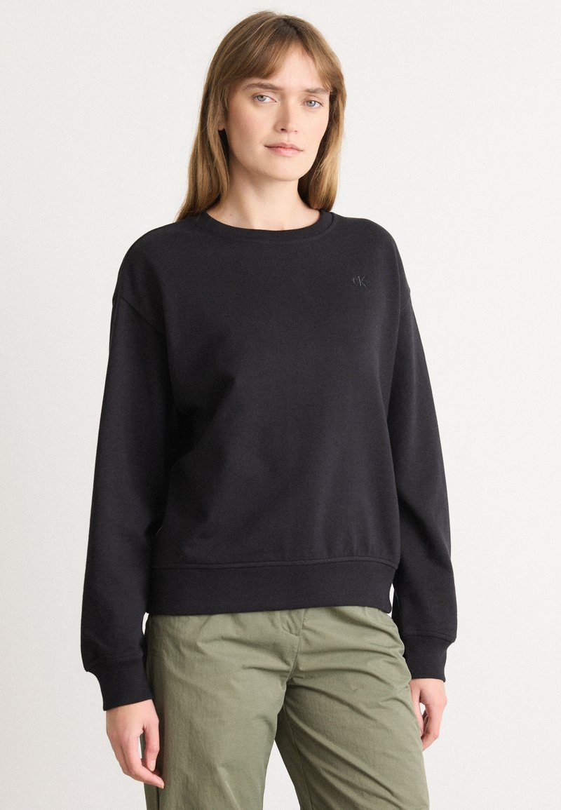 Čierny crewneck sveter s rebrovanými manžetami a lemovaním, s nen�ápadným logom na hrudi. Vyrobený z mäkkej zmesi bavlny.