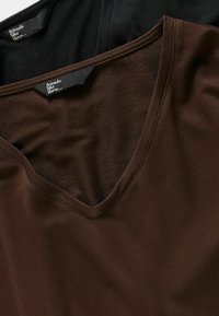 Dvije majice s V-izrezom složene jedna na drugu: jedna crna i jedna smeđa. Tkanina ima glatku teksturu s vidljivim šavovima uz izrez na vratu.