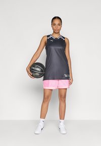 Musthave musta ilma varrukatega korvpallivorm koos valgete detailidega, kombinatsioonis roosade võrkkudumist lühikestega; hoiab käes musta Spalding korvpalli.