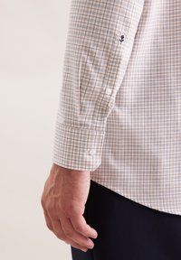 Camicia a quadri chiari con un motivo beige e bianco, polsino abbottonato con due bottoni bianchi e delicate ricamo floreale sulla manica.