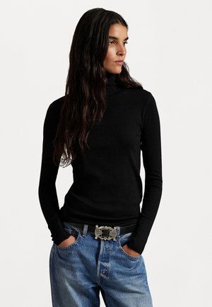 Melna garām piedurknēm turtlenecka blūze no ribota auduma, saskaņota ar augsto jostasvietu ziliem džinsiem un melnu jostu ar sudraba akcentiem.