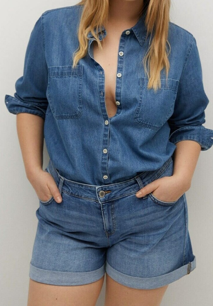 Camisa azul de mezclilla con cierre de botones y dos bolsillos en el pecho, combinada con pantalones cortos de mezclilla azul claro con dobladillos enrollados y bolsillos delanteros.