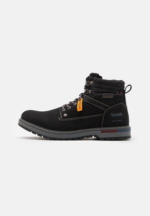 Botas negras hasta el tobillo con un upper de tela texturizada y suela de goma gris. Cuenta con ojales de metal, un cuello de punto y una etiqueta de marca naranja.