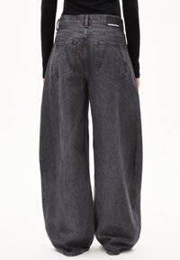 Schwarze Denim-Jeans mit weitem Bein und hoher Taille, mit einem Etikett hinten, zwei Gesäßtaschen und einer strukturierten Oberfläche.