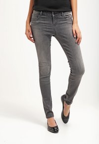 Jeans skinny de denim gris con un acabado ligeramente desgastado, diseño de cinco bolsillos y cintura de tiro medio, combinados con bailarinas negras.