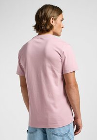 Lyserød T-shirt med korte �ærmer lavet af bomuld, med rund hals og ensfarvet design, iført sammen med lyseblå denimbukser.