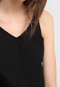 Black sleeveless top with a v-neck and textured fabric featuring small raised patterns, shown against a neutral background.